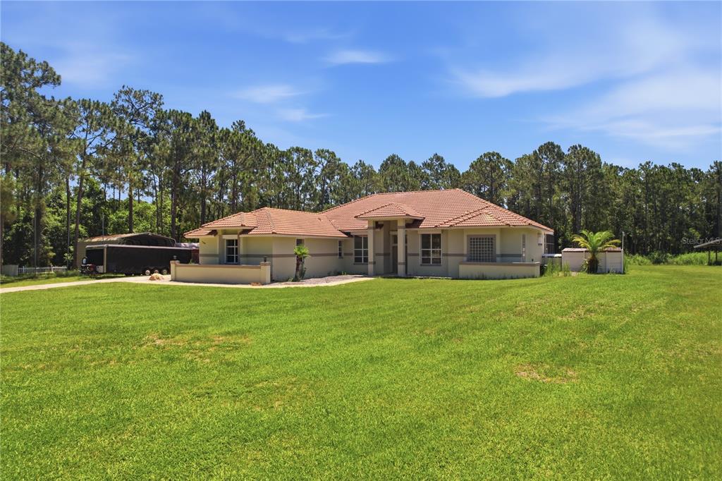 A single-story house with a tiled roof sits on a large grassy lot near trees — 7190 SIX GUN COURT, ST CLOUD, FL