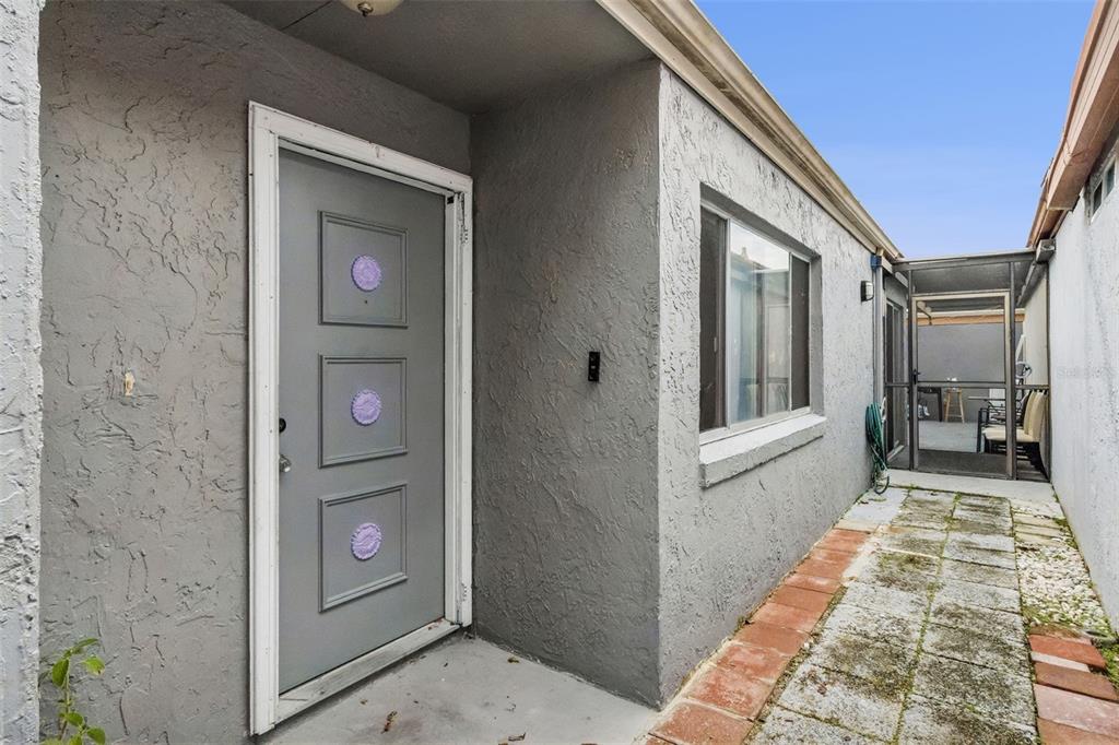 A gray front door with three purple accents sits beside a window and paved walkway — 271 MARIPOSA, WINTER HAVEN, FL