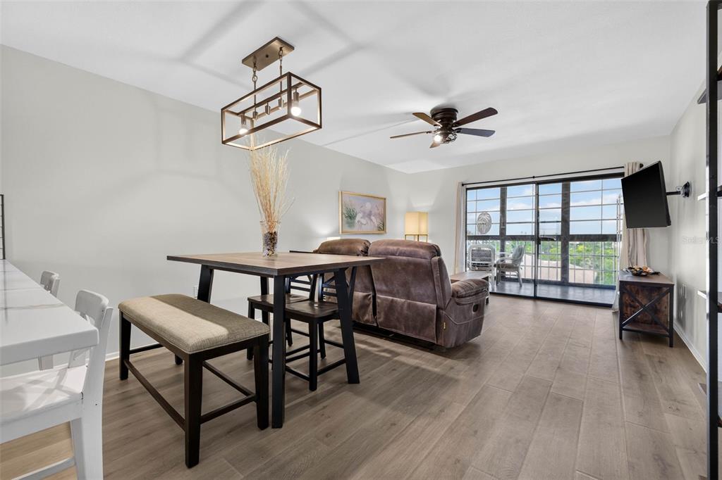 A dining area with a wooden table and bench opens into a living room with sliding doors — 9860 62ND TERRACE N UNIT 1048, ST PETERSBURG, FL