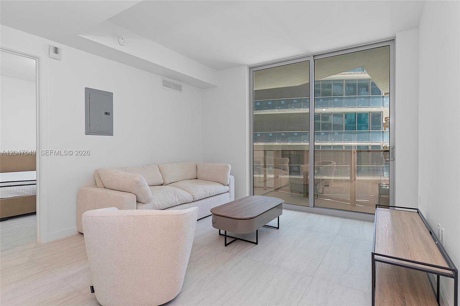 A living room with a beige sofa, armchair, coffee table, and sliding glass balcony doors — 77 SE 5th St. # 1905, Miami FL 33131, MIAMI, FL