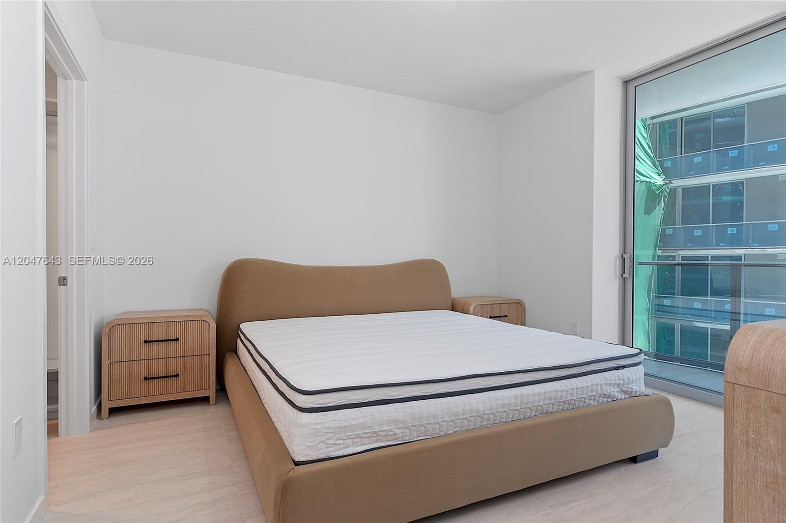 A bedroom features a tan upholstered bed, two wooden nightstands, and a glass balcony door — 77 SE 5th St. # 1905, Miami FL 33131, MIAMI, FL