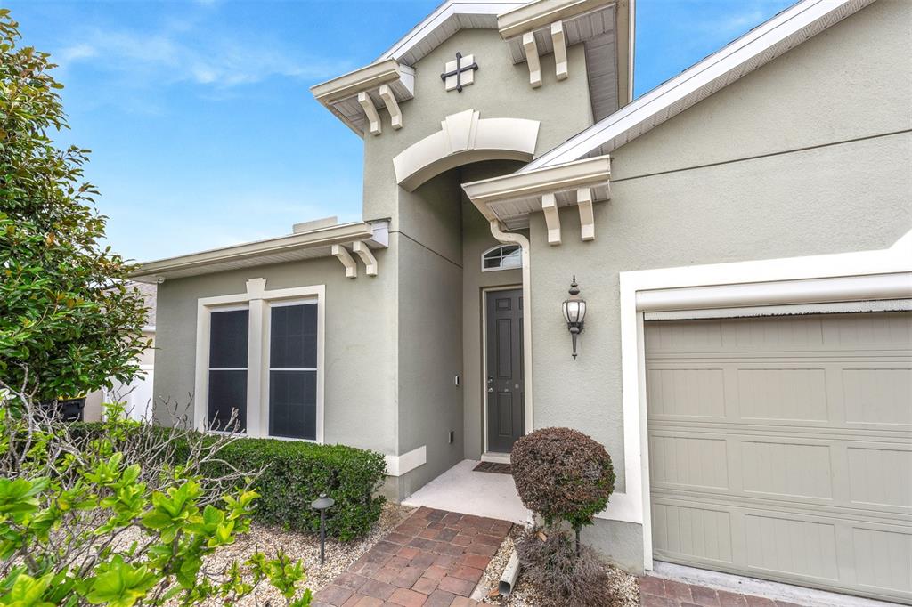 A single-story house exterior features a gray stucco facade, a dark front door, and garage — 980 GLAZEBROOK LOOP, ORANGE CITY, FL