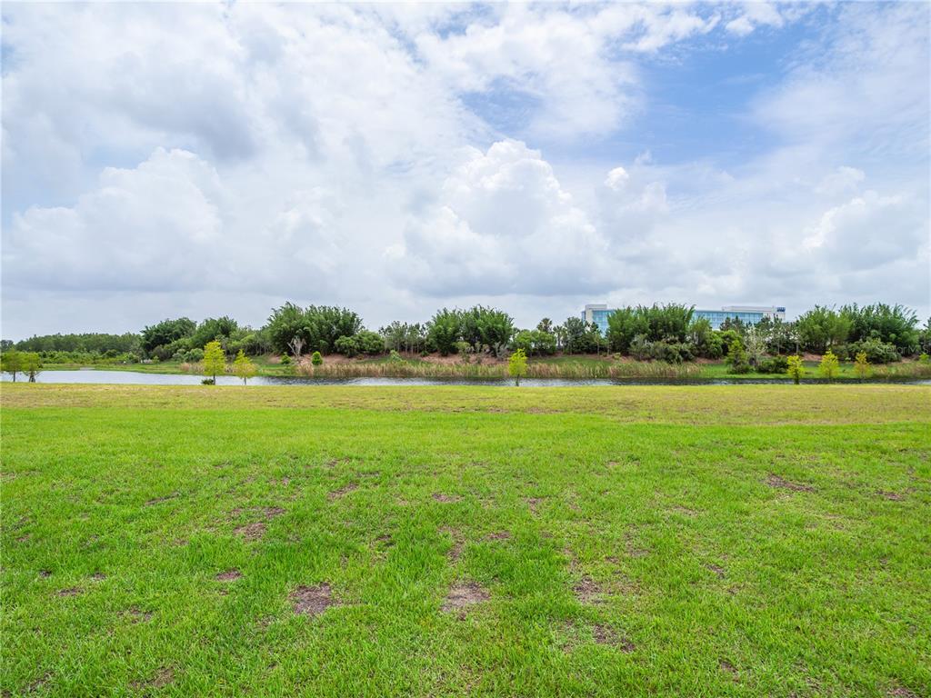 A grassy field overlooks a pond with a line of trees and a building beyond — LOT 36, CROMWELL ROAD, ORLANDO, FL