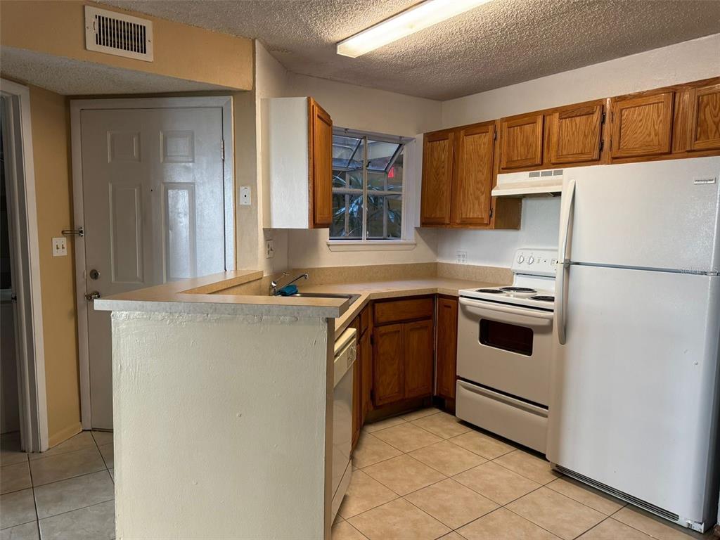 A kitchen features wood cabinets, white appliances, a tiled floor, and a breakfast bar — 1940 LAKE ATRIUMS CIRCLE UNIT 107, ORLANDO, FL