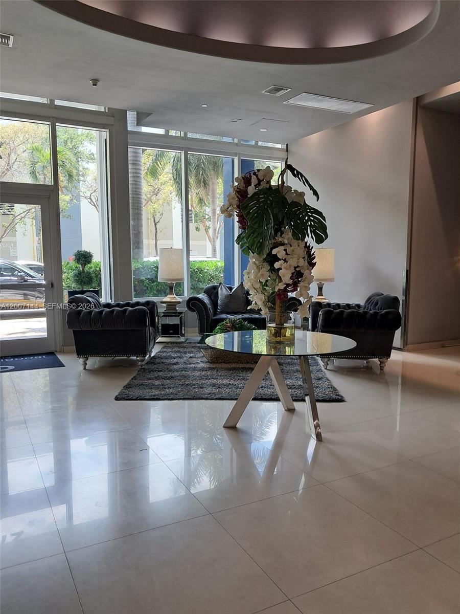A modern lobby features a glass table, dark tufted armchairs, and floor-to-ceiling windows — 275 NE 18th St # 1704, Miami FL 33132, MIAMI, FL