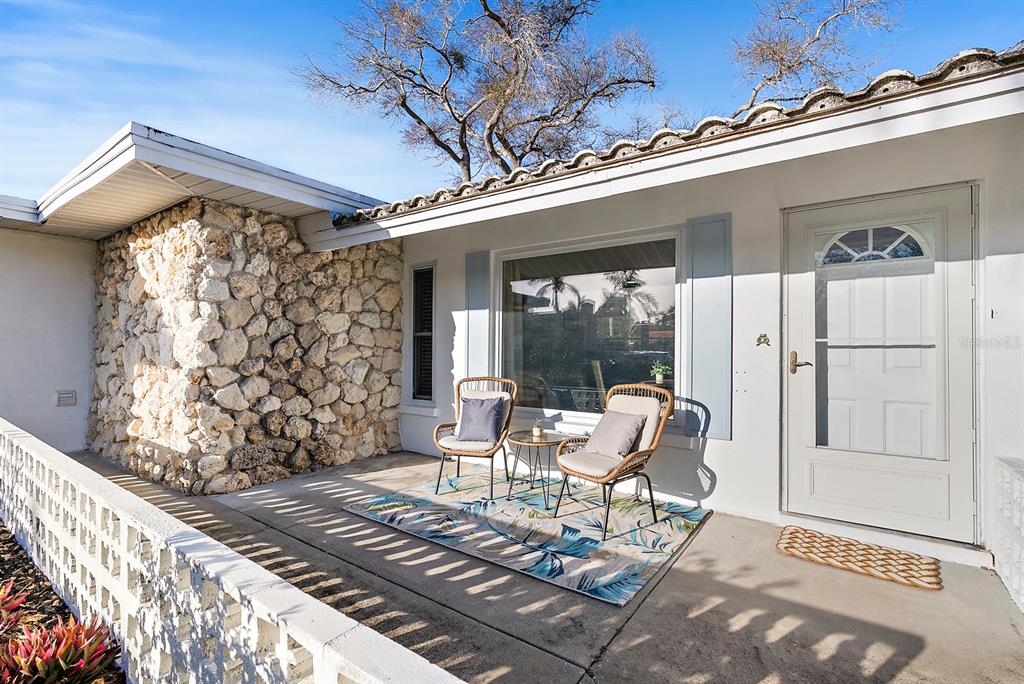 A front porch features a stone accent wall, two wicker chairs, and a patterned rug — 514 HARBOR DRIVE S, VENICE, FL