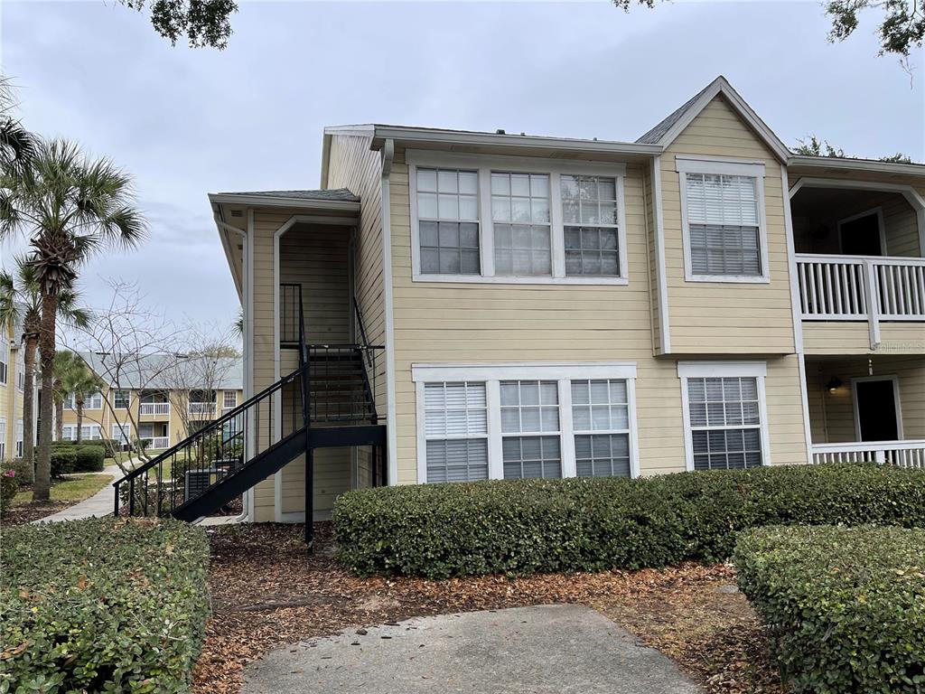 A two-story apartment building exterior features light yellow siding, a metal staircase, and landscaping — 1027 S HIAWASSEE ROAD UNIT 2311, ORLANDO, FL