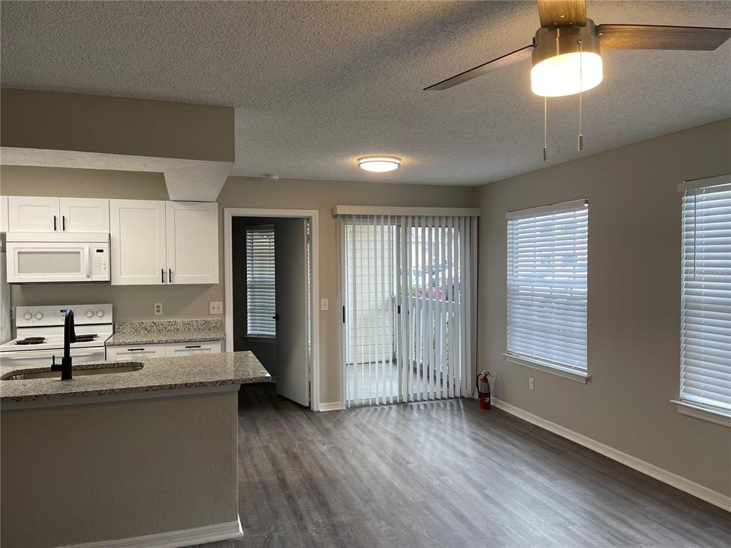 A kitchen with white cabinets and granite countertops opens into a living area with flooring — 1027 S HIAWASSEE ROAD UNIT 2311, ORLANDO, FL