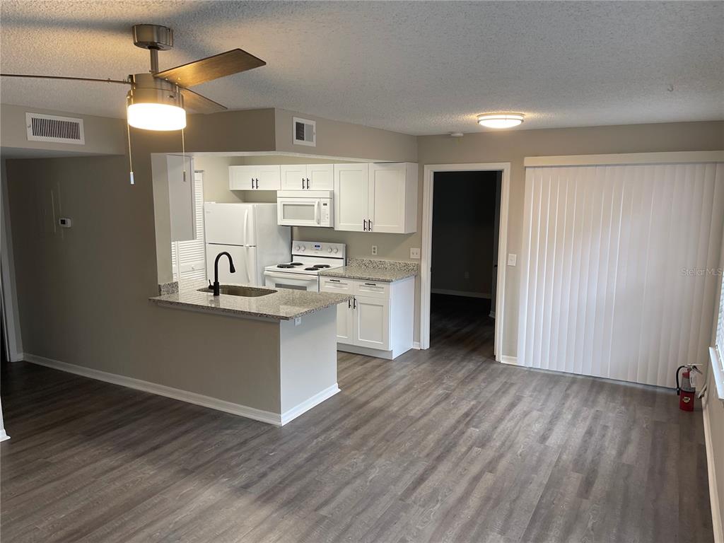 A kitchen with white cabinets and granite countertops opens into a living area with flooring — 1027 S HIAWASSEE ROAD UNIT 2311, ORLANDO, FL