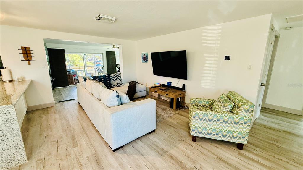 A living room features a white sectional sofa, patterned armchair, and a wall-mounted television — 4926 BLUE HERON DRIVE, NEW PORT RICHEY, FL