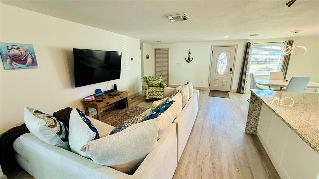 A living room features a large sectional sofa, a wall-mounted television, and light wood flooring — 4926 BLUE HERON DRIVE, NEW PORT RICHEY, FL