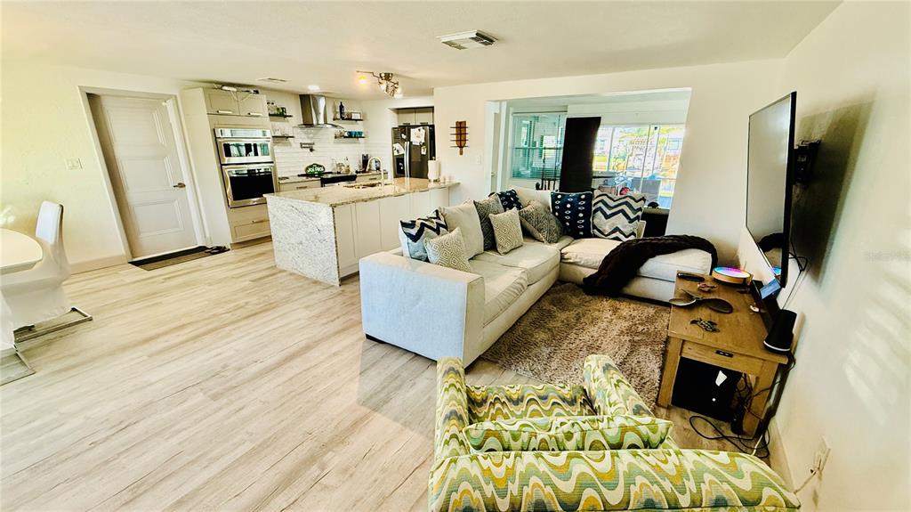 An open-concept living room and kitchen featuring light wood floors and white cabinetry — 4926 BLUE HERON DRIVE, NEW PORT RICHEY, FL