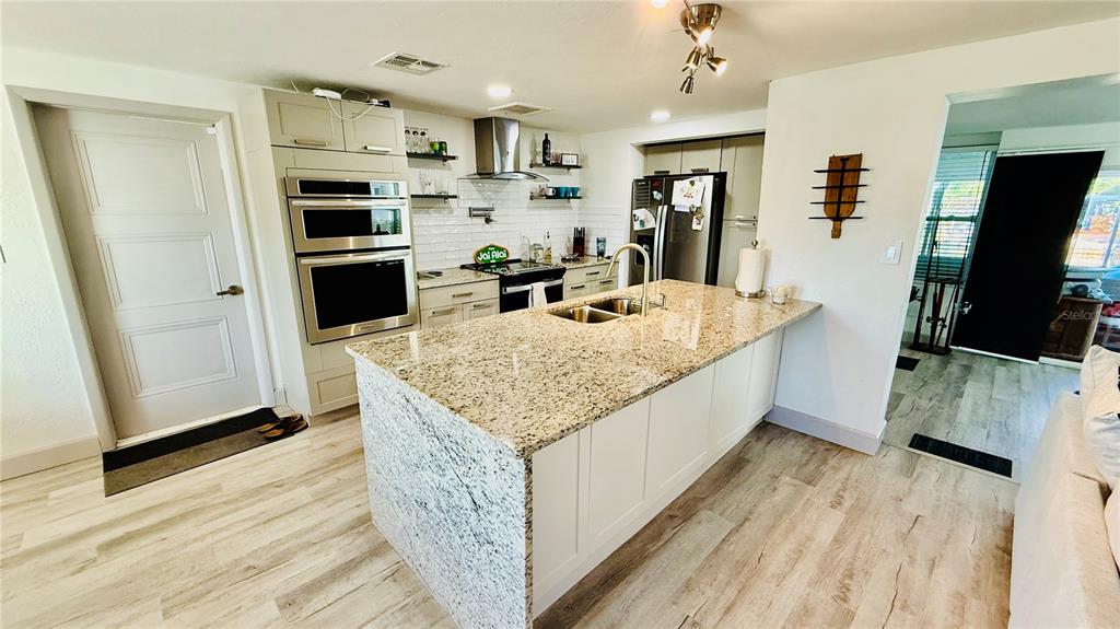 A kitchen features a granite-topped island, white cabinetry, stainless steel appliances, and light wood flooring — 4926 BLUE HERON DRIVE, NEW PORT RICHEY, FL