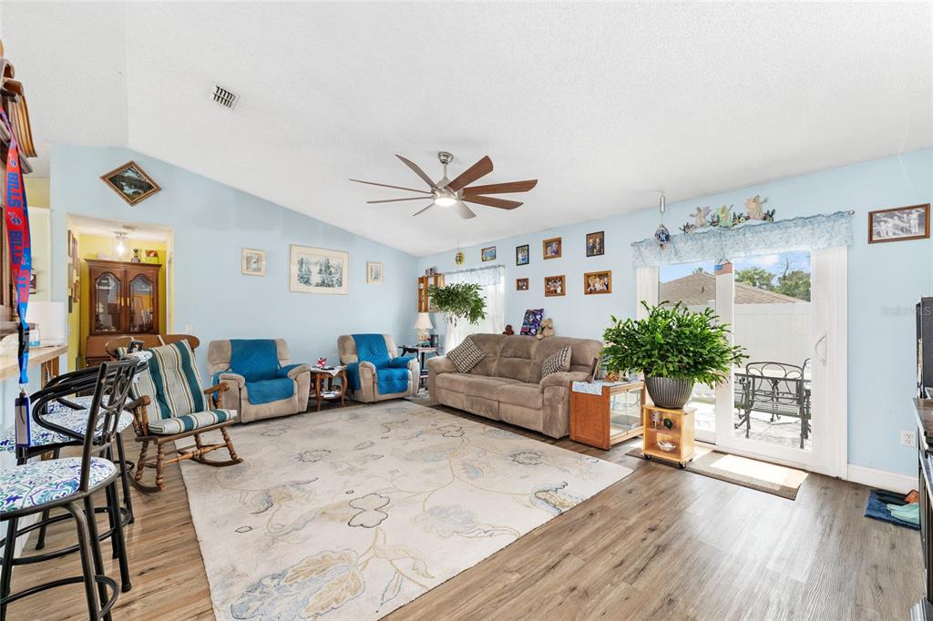 A living room with light blue walls, wood-look flooring, a ceiling fan, and sliding glass doors — 124 OAK CIRCLE, OCALA, FL