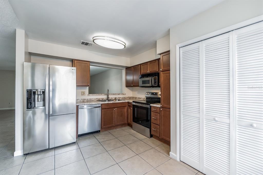 A kitchen features stainless steel appliances, wood cabinets, tile flooring, and a pass-through window — 2748 CANDLEWOOD COURT, APOPKA, FL