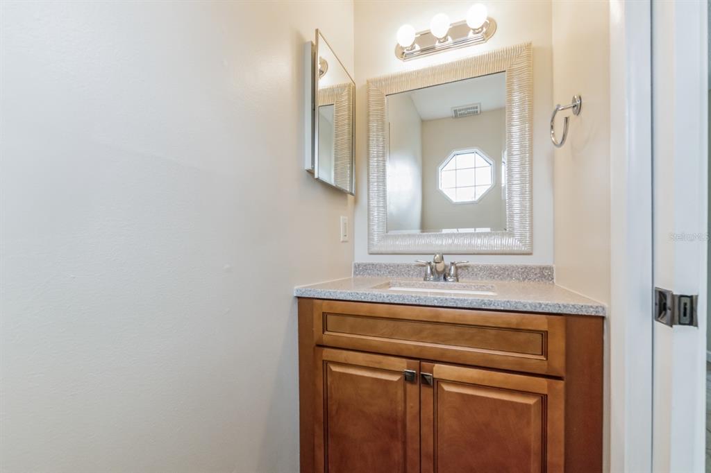 A bathroom features a wooden vanity with a stone countertop, a mirror, and light fixtures — 2748 CANDLEWOOD COURT, APOPKA, FL