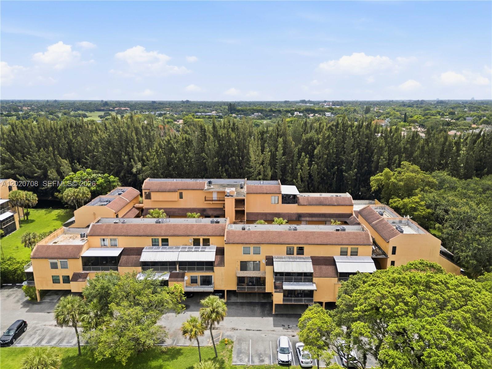 An aerial view shows a multi-story yellow apartment complex surrounded by trees and parking lots — 430 Commodore Dr # 213, Plantation FL 33325, PLANTATION, FL