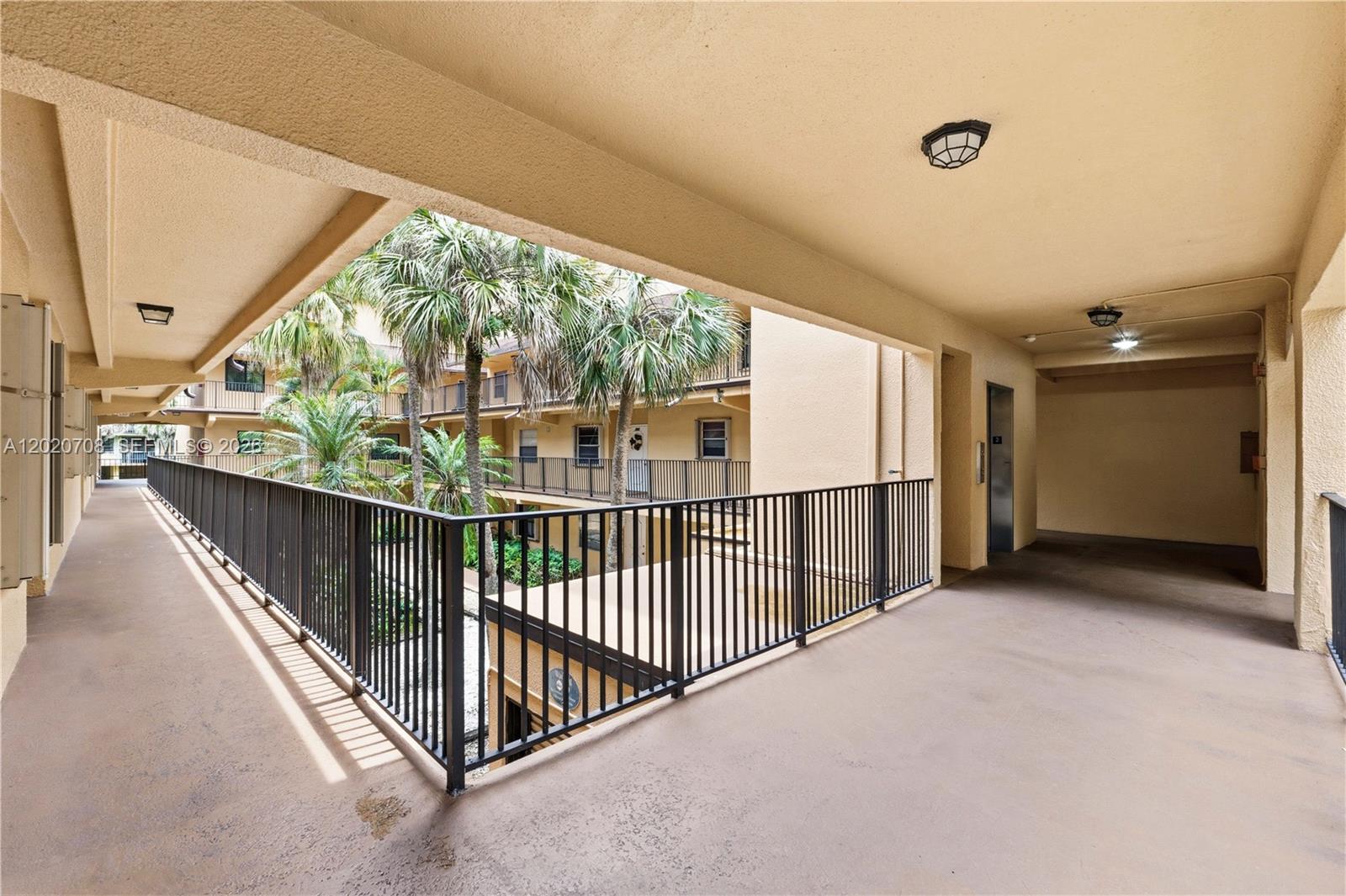An open-air walkway with black metal railings overlooks a courtyard with palm trees — 430 Commodore Dr # 213, Plantation FL 33325, PLANTATION, FL