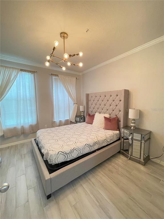 A bedroom features a tufted headboard, mirrored nightstand, chandelier, and light-colored wood-look tile flooring — 4221 W SPRUCE STREET UNIT 1107, TAMPA, FL