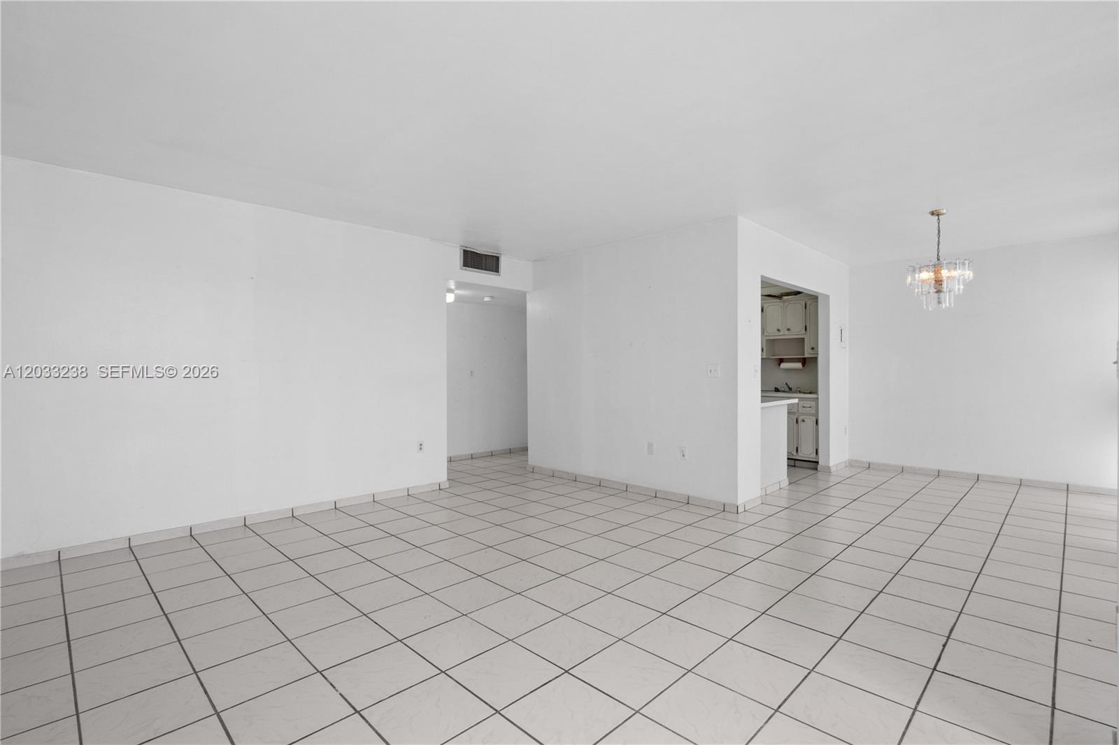 An empty room features white walls, white tile flooring, and a crystal chandelier — 8001 Byron Ave # 3C, Miami Beach FL 33141, MIAMI BEACH, FL
