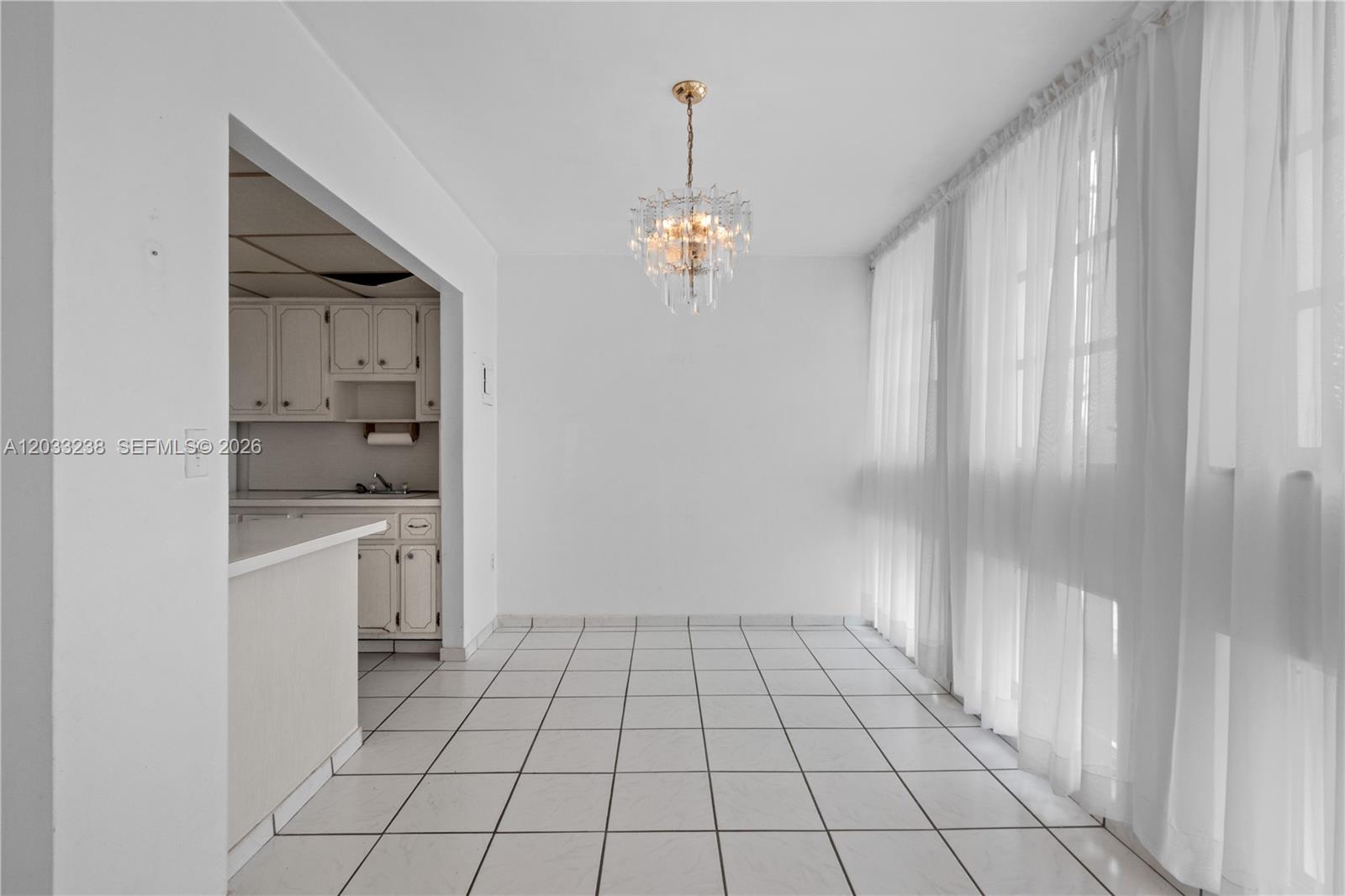 A dining area features white tile flooring, a crystal chandelier, and large windows with curtains — 8001 Byron Ave # 3C, Miami Beach FL 33141, MIAMI BEACH, FL