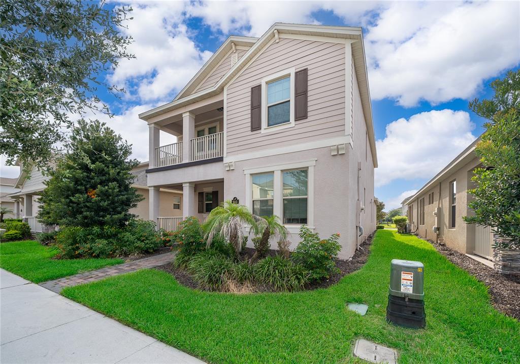 A two-story house with beige siding and stucco features a front balcony and landscaped yard — 9445 KOMIKA LANE, WINTER GARDEN, FL