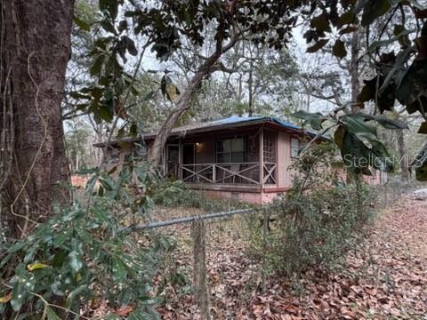 A single-story house with a front porch sits behind a chain-link fence among trees — 7415 BERNADETTE DRIVE, NAVARRE, FL