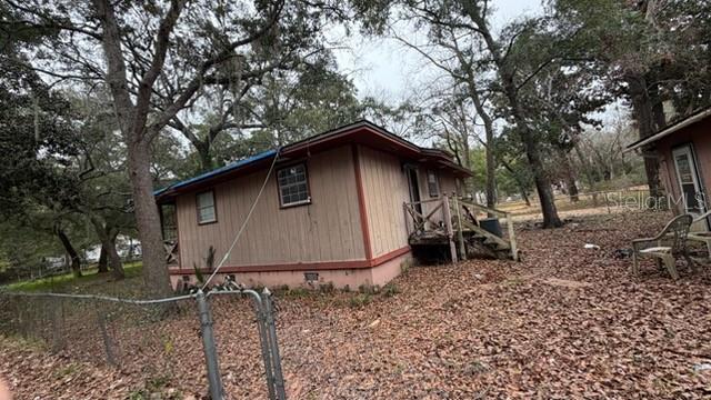 A tan, single-story house with red trim sits on a lot covered in fallen leaves — 7415 BERNADETTE DRIVE, NAVARRE, FL