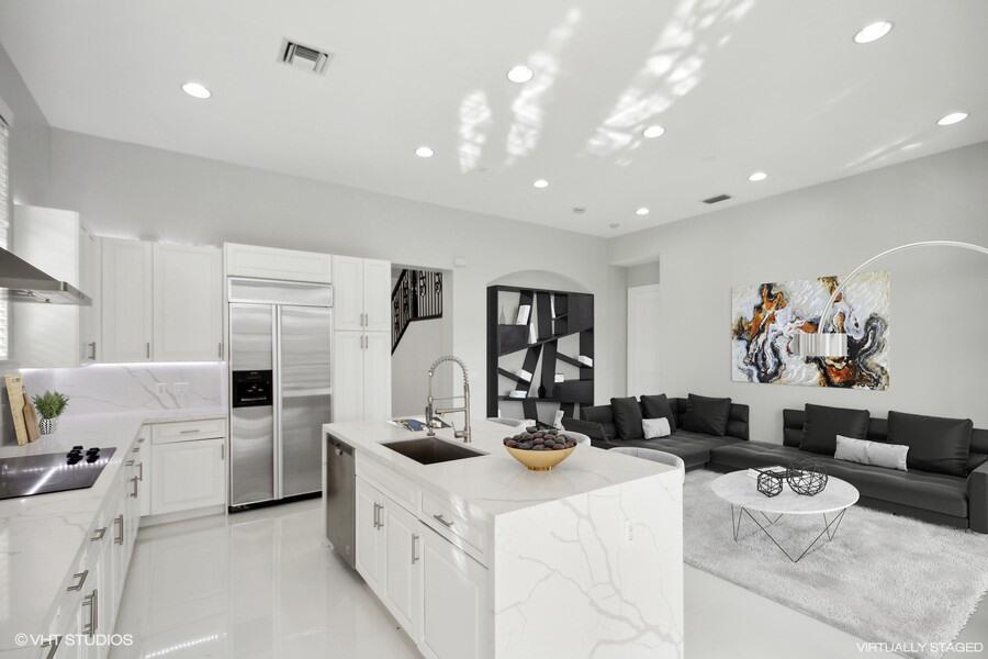 A modern open-concept kitchen and living area featuring white cabinetry, marble countertops, and black furniture — 9648 Ginger Court, Parkland FL 33076, PARKLAND, FL
