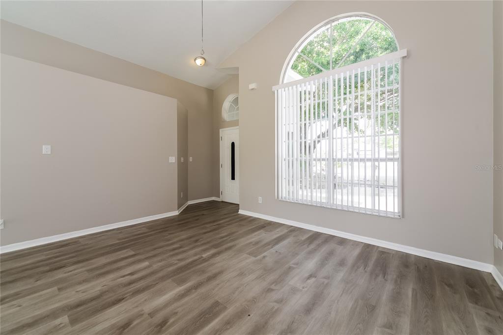 An empty room with light-colored walls, wood-look flooring, and a large arched window with blinds — 1003 DORKING WAY, KISSIMMEE, FL
