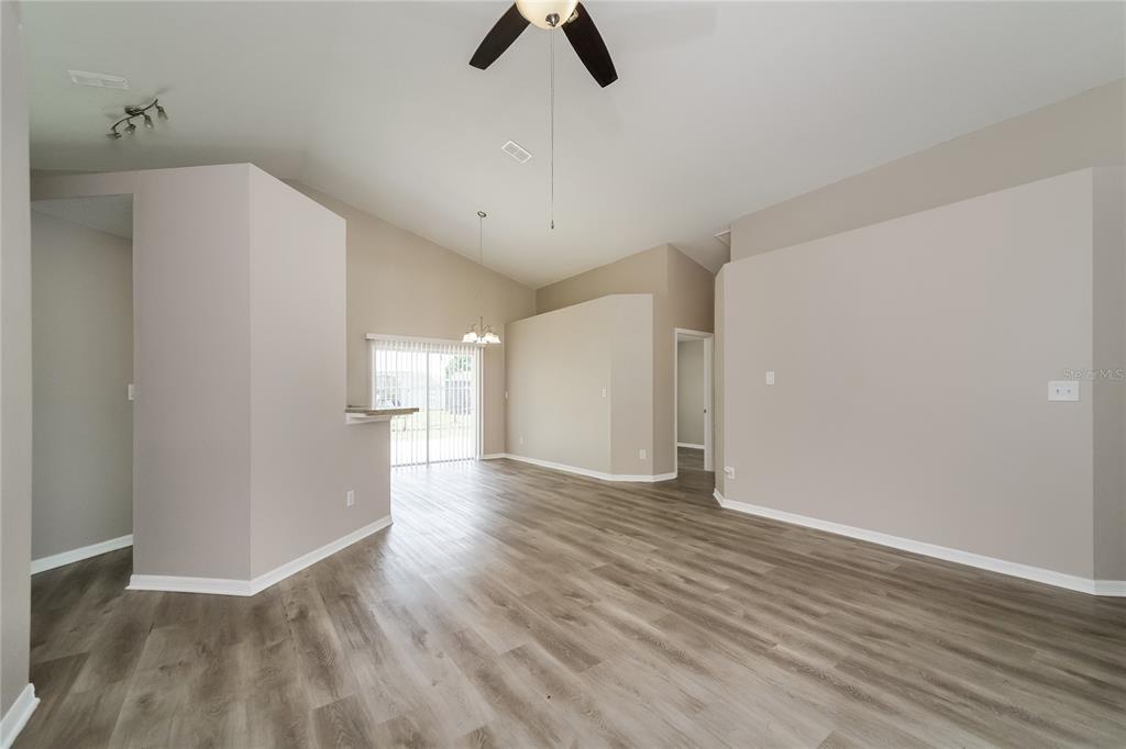 An open-concept living area features light gray walls, wood-look flooring, and a vaulted ceiling — 1003 DORKING WAY, KISSIMMEE, FL