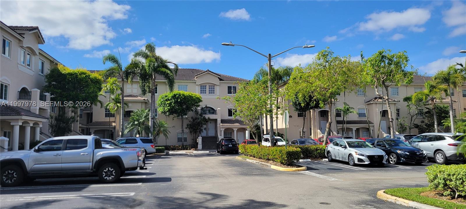 A parking lot sits in front of multi-story residential buildings with palm trees and landscaping — 5640 NW 115th Ct # 211, Doral FL 33178, DORAL, FL