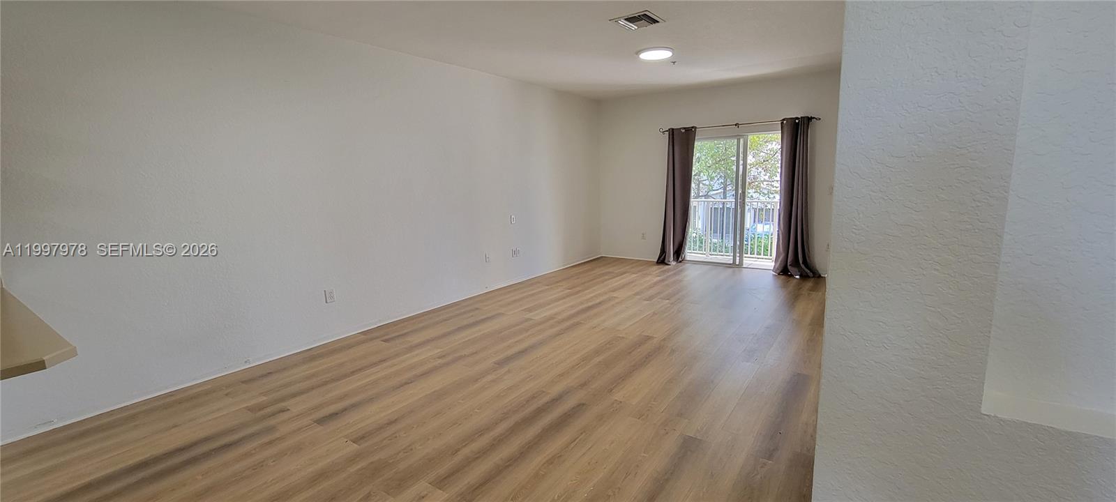 An empty living room features light wood-look flooring, white walls, and a sliding glass door — 5640 NW 115th Ct # 211, Doral FL 33178, DORAL, FL