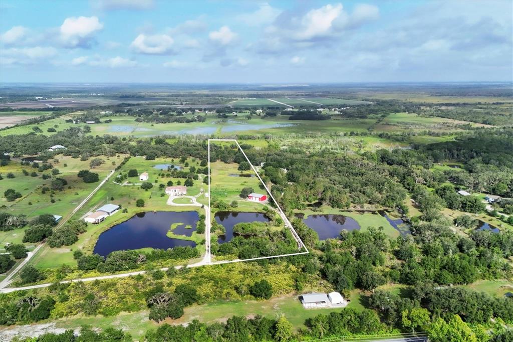 An aerial view of a red metal workshop building situated on a large grassy lot — 3045 LOGUE ROAD, MYAKKA CITY, FL