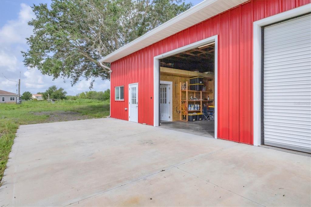 A red metal workshop building features a concrete apron, a roll-up door, and a side entrance — 3045 LOGUE ROAD, MYAKKA CITY, FL