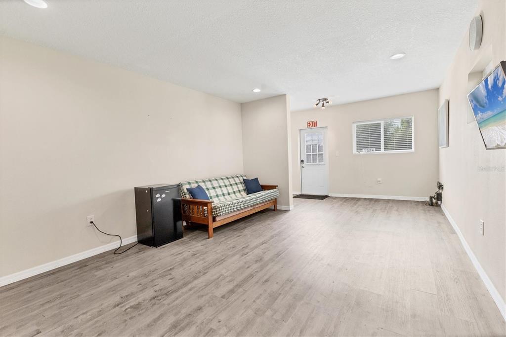 A living room with light-colored walls, wood-look flooring, a futon, and a small refrigerator — 3045 LOGUE ROAD, MYAKKA CITY, FL