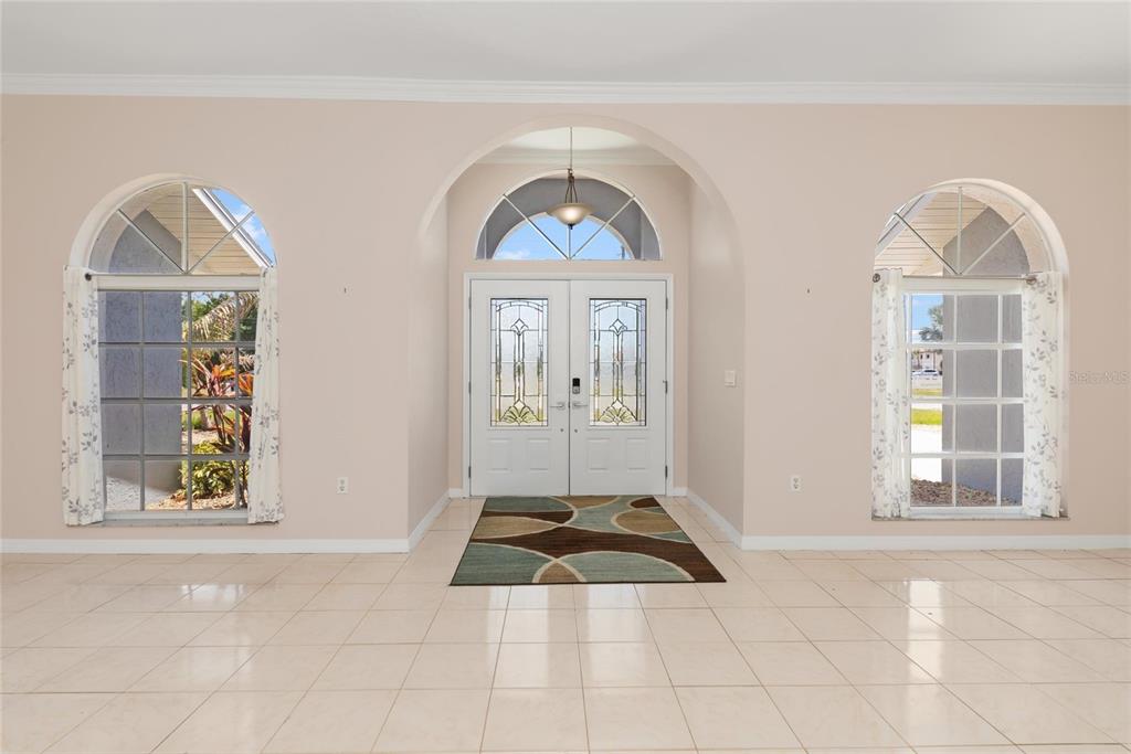 A bright foyer features white double doors, arched windows, and light-colored tile flooring — 25332 RAMPART BOULEVARD, PUNTA GORDA, FL