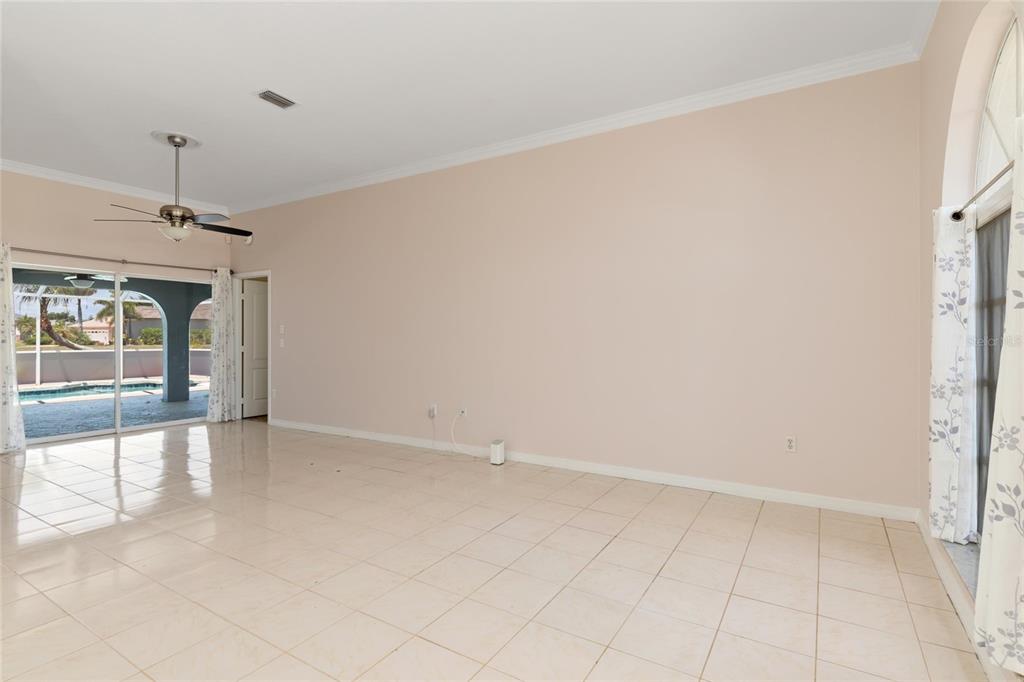 A spacious living room features light-colored tile flooring, beige walls, and sliding glass patio doors — 25332 RAMPART BOULEVARD, PUNTA GORDA, FL