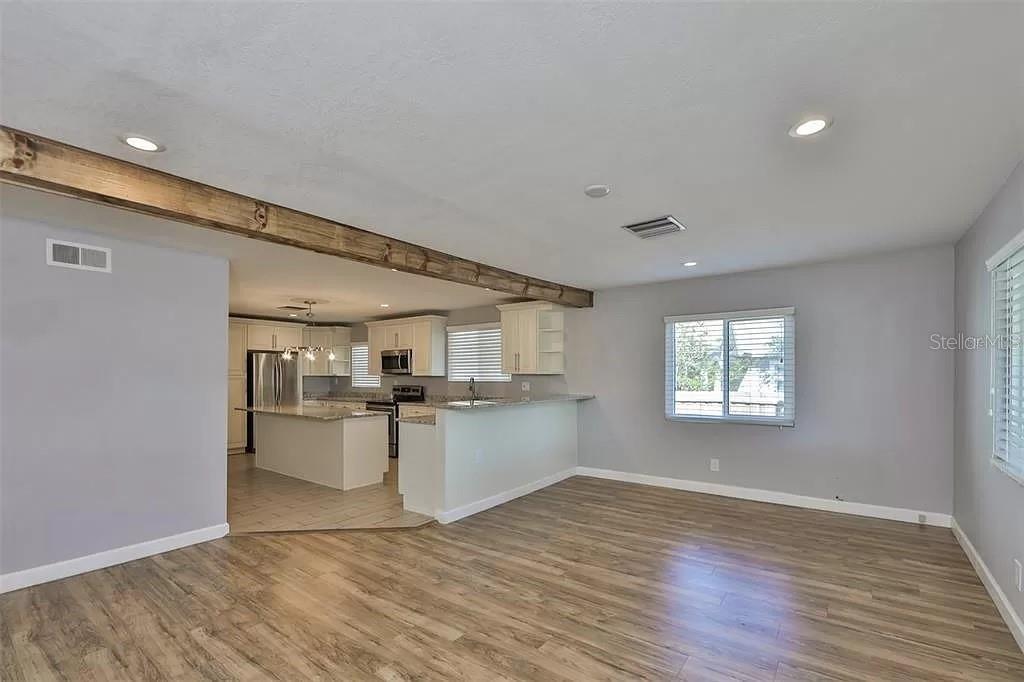 An open-concept kitchen and living area feature wood-look flooring and a rustic ceiling beam — 3219 W LEROY STREET, TAMPA, FL