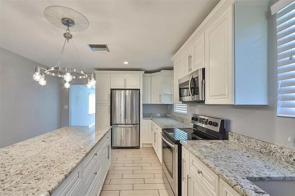 A kitchen features white cabinets, granite countertops, stainless steel appliances, and a pendant chandelier — 3219 W LEROY STREET, TAMPA, FL