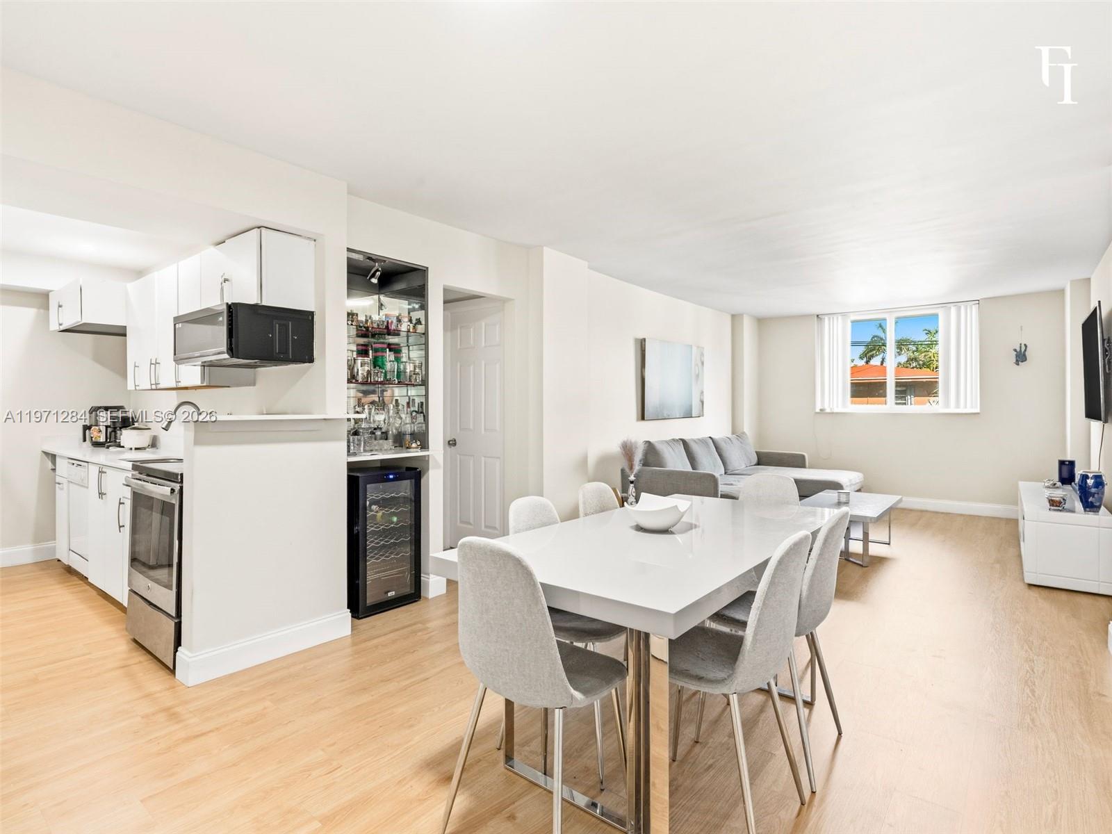 An open-concept living and dining area features a white kitchen, wine cooler, and light flooring — 1251 NE 108th St # 108, Miami FL 33161, MIAMI, FL