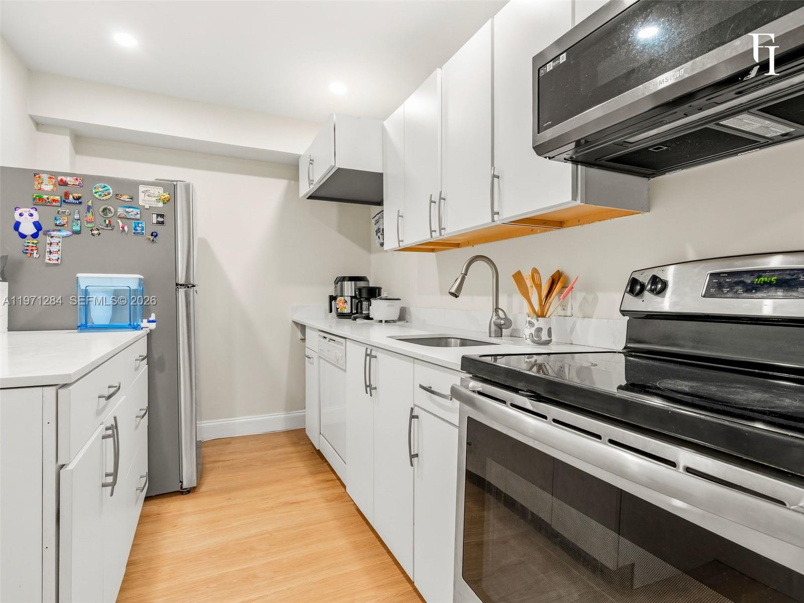 A kitchen features white cabinets, stainless steel appliances, and light wood-look flooring — 1251 NE 108th St # 108, Miami FL 33161, MIAMI, FL
