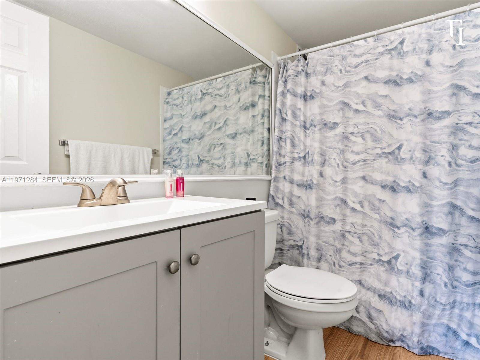 A bathroom features a gray vanity, white countertop, brushed nickel faucet, and a blue-patterned shower curtain — 1251 NE 108th St # 108, Miami FL 33161, MIAMI, FL