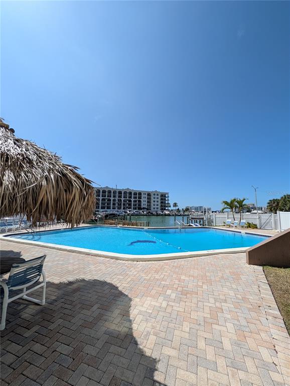 A swimming pool with a tiki hut and patio overlooks a bay and large building — 255 DOLPHIN POINT UNIT 505, CLEARWATER BEACH, FL