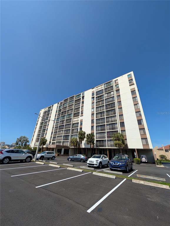 A multi-story apartment building stands behind a parking lot with several parked cars — 255 DOLPHIN POINT UNIT 505, CLEARWATER BEACH, FL