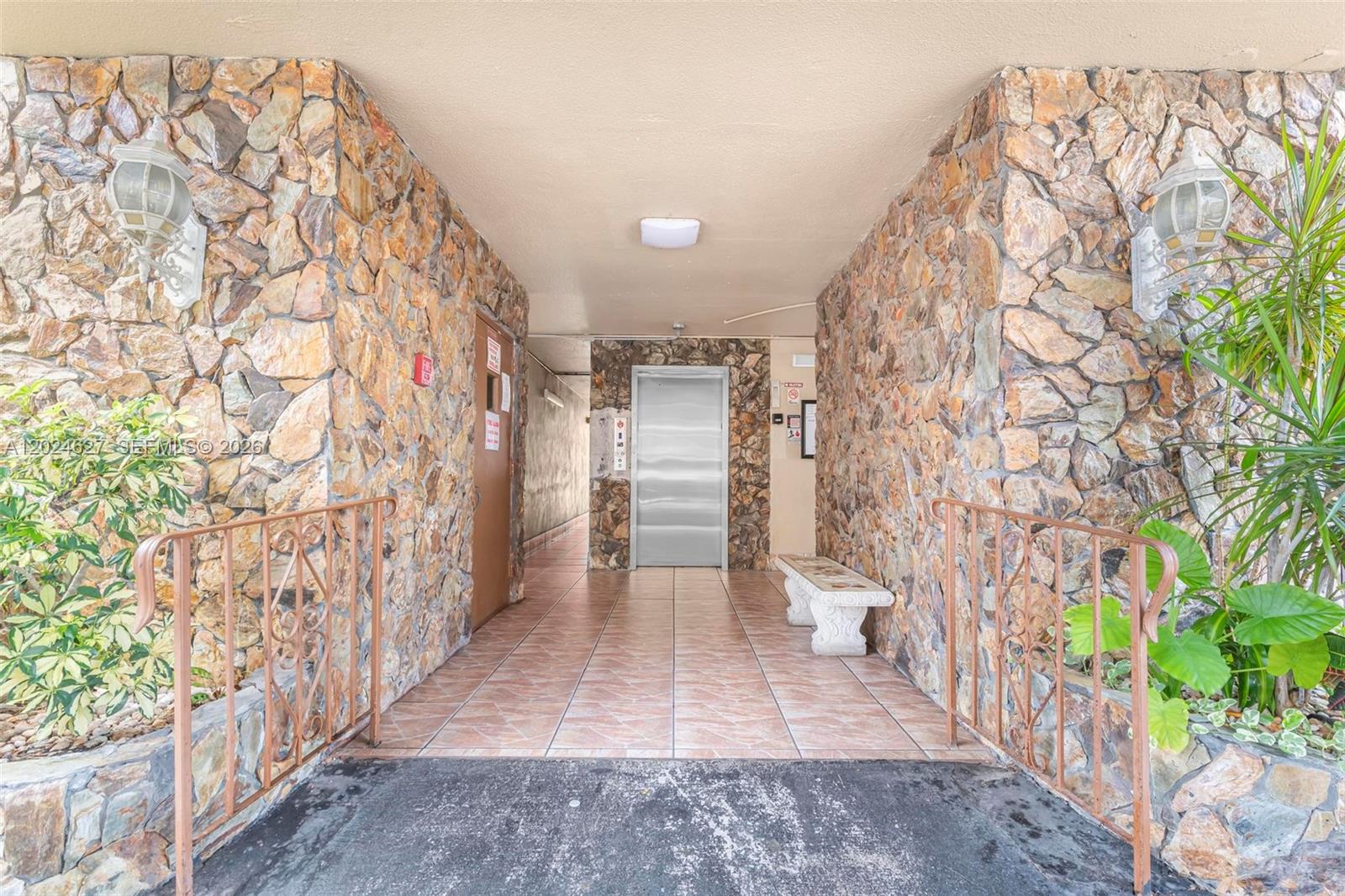 An outdoor entryway features stone walls, a tiled floor, a metal railing, and an elevator — 500 NE 12th Ave # 407, Hallandale Beach FL 33009, HALLANDALE BEACH, FL