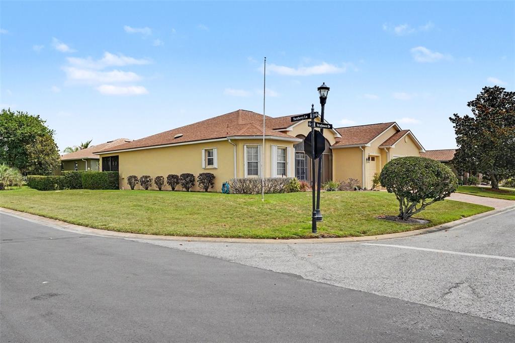 A yellow single-story house sits on a corner lot with a street sign and lamp — 4496 STRATHMORE DRIVE, LAKE WALES, FL