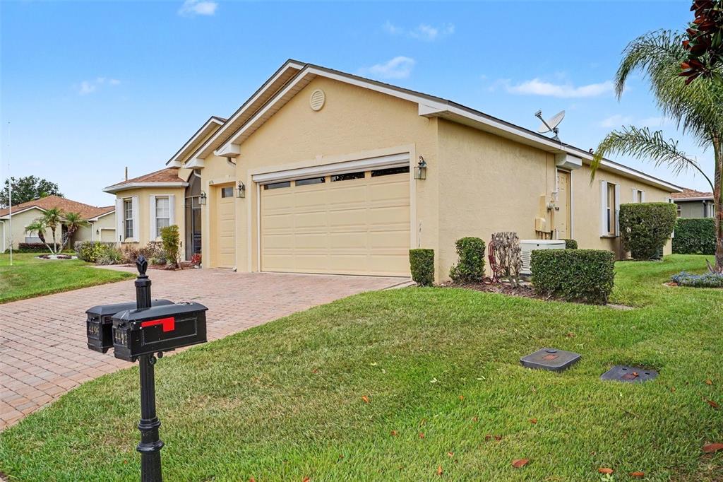 A single-story house with a beige stucco exterior, a two-car garage, and a brick driveway — 4496 STRATHMORE DRIVE, LAKE WALES, FL