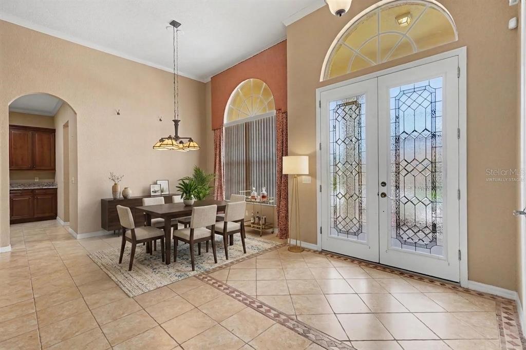A dining area with tile floors, a wooden table, and double glass-paneled front doors — 4496 STRATHMORE DRIVE, LAKE WALES, FL