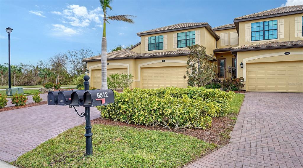 A multi-unit residential building with a paved driveway, a mailbox post, and a palm tree — 6512 GRAND ESTUARY TRAIL UNIT 102, BRADENTON, FL
